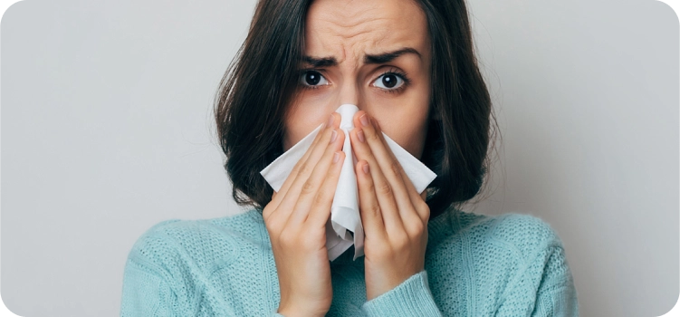 الصورة: امرأة مصابة بنزلة برد وتمسك منديلًا